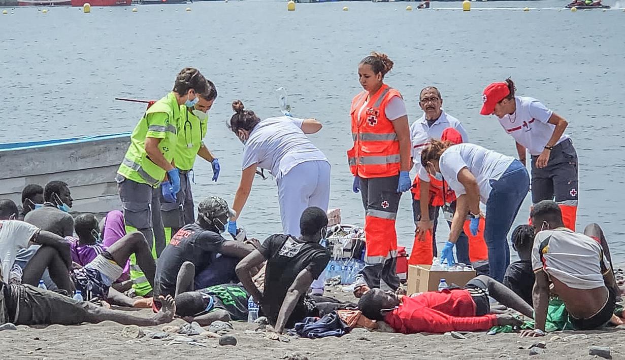 Foto selebaran yang dirilis oleh Palang Merah Spanyol (Cruz Roja) pada 13 Juli 2023 menunjukkan anggota Palang Merah dan responden pertama merawat orang-orang setelah sebuah kapal tiba dengan 41 migran di dalamnya, di pantai Las Galletas di kotamadya Arona, di Pulau Canary Tenerife. (Handout / SPANISH RED CROSS / AFP)