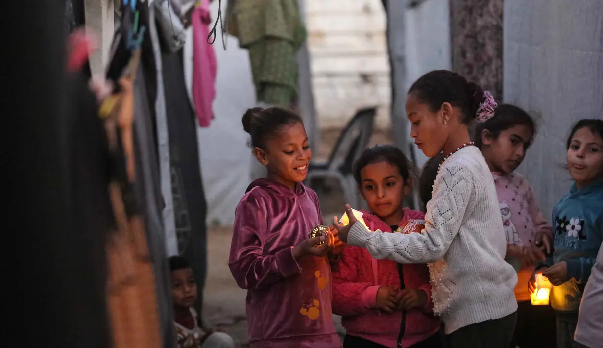 Bagi mereka dan keluarga yang tinggal di lokasi pengungsian, tradisi menyambut Ramadan tetap dijaga sebisanya. Tampak dalam foto, para pengungsi muda Palestina bermain dengan lampion Ramadan saat dekorasi dipasang di samping tenda mereka di kamp pengungsi Bureij di Jalur Gaza tengah pada 15 Februari 2026. (Eyad Baba/AFP)