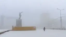 Seorang perempuan berjalan melewati patung pendiri Uni Soviet Vladimir Lenin saat suhu turun hingga sekitar minus 50 derajat Celcius (-58 derajat Fahrenheit) di Yakutsk, Rusia, Sabtu (16/1/2021).  Yakutsk atau Yakutia tersohor sebagai kota terdingin di dunia. (AP Photo/Ajar Warlamov)