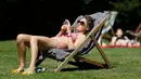 Seorang wanita berjemur di atas terik matahari di Regents Park sambil bermain ponsel, London, Inggris, Selasa (19/7). Inggris tengah dilanda gelombang panas dengan suhu 35 derajat celcius. (REUTERS/Neil Hall)