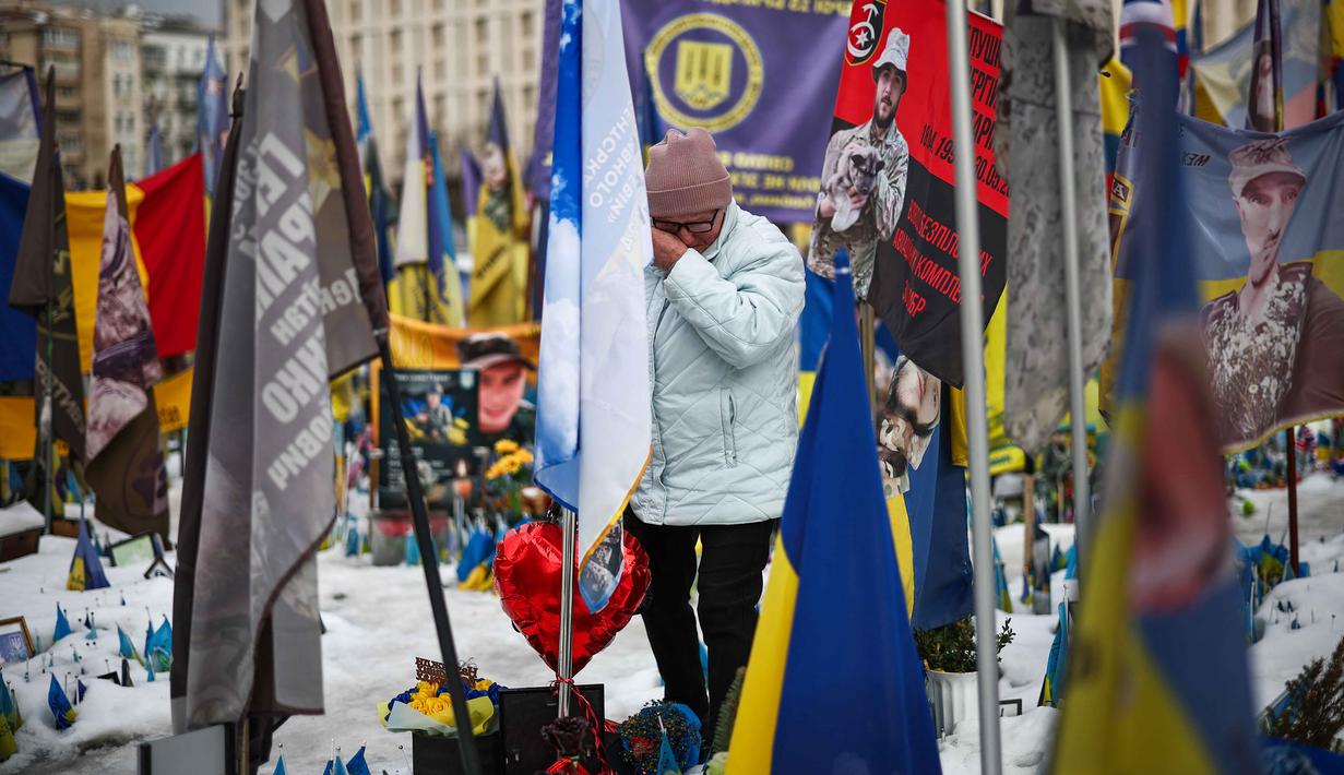 Perang antara Rusia dan Ukraina berdampak pada krisis kemanusiaan dan ekonomi yang sangat besar. Tampak dalam foto, seorang warga setempat bereaksi saat mengunjungi tugu peringatan sementara untuk tentara Ukraina dan asing di Lapangan Kemerdekaan, Kyiv, saat peringatan keempat invasi Rusia ke Ukraina, Selasa 24 Februari 2026. (HENRY NICHOLLS/AFP)