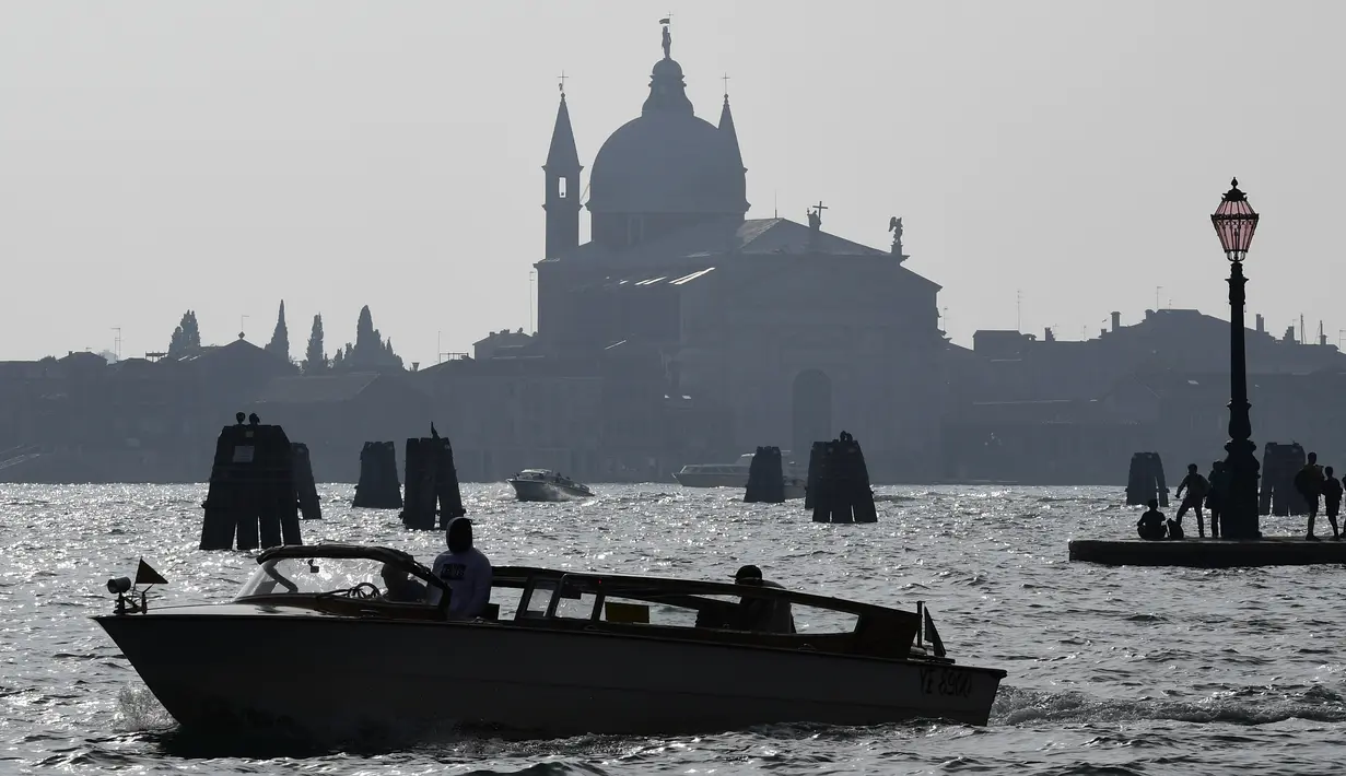 Gereja Santa Croce terlihat di pulau Giudecca dan orang-orang berdiri di Punta della di Venesia (4/11/2019). Punta della Dogana adalah sebuah museum seni di salah satu bangunan pabean lama Venesia, Dogana da Mar. (AFP Photo/Miguel Medina)