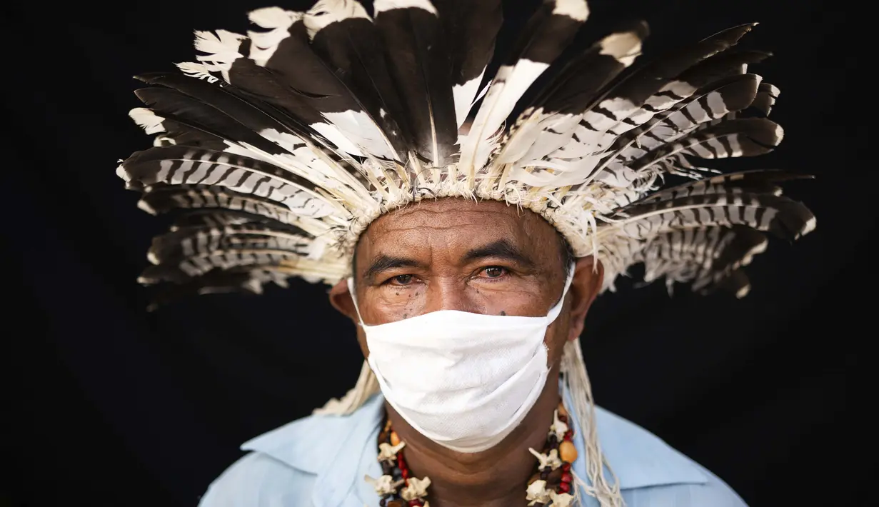 Pemimpin adat dari etnis Mura, Pedro dos Santos memakai pakaian tradisional dan masker saat pandemi virus corona COVID-19 di Taman Bangsa Adat, Manaus, Brasil, Kamis (28/5/2020). Pada bulan April, dos Santos, istri, anak-anak, dan cucunya jatuh sakit dengan gejala COVID-19. (AP Photo/Felipe Dana)