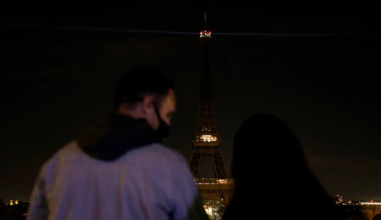 Orang-orang melihat lampu Menara Eiffel di Paris, yang dimatikan pada Rabu (21/10/2020). Kondisi gelap gulita itu untuk memberikan penghormatan terhadap Samuel Paty, seorang guru sejarah yang dipenggal kepalanya pada Jumat (16/10) lalu. (GEOFFROY VAN DER HASSELT / AFP)