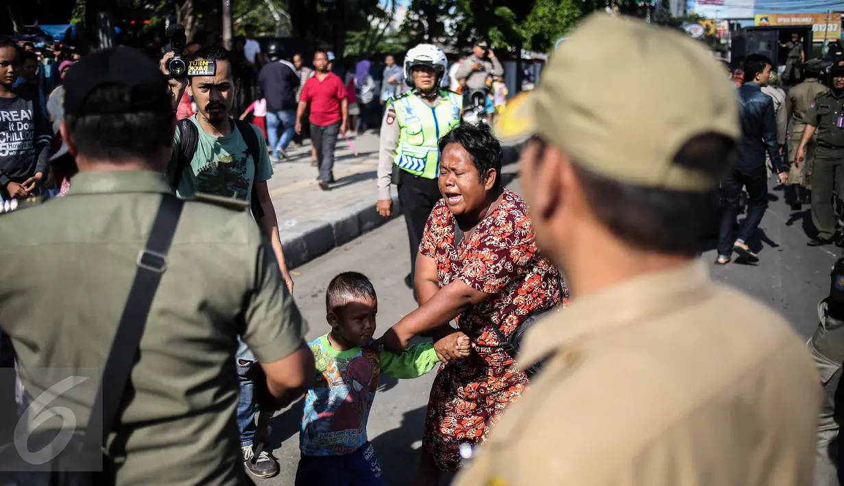 Seorang ibu bersama anaknya pemilik gerobak yang diamankan melawan dalam penertipan pedagang kaki lima (PKL) di kawasan Stasiun Kota Tua, Jakarta, Selasa (25/10). (Liputan6.com/Faizal Fanani)