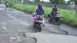 Pengendara sepeda motor melintasi jalan yang rusak di Jalan Raya Gas Alam, Depok, Jawa Barat, Selasa (7/5). Kondisi jalan yang tidak kunjung diperbaiki tersebut menjadi kubangan air setiap hujan serta berbahaya bagi keselamatan pengguna jalan. (Liputan6.com/Immanuel Antonius)