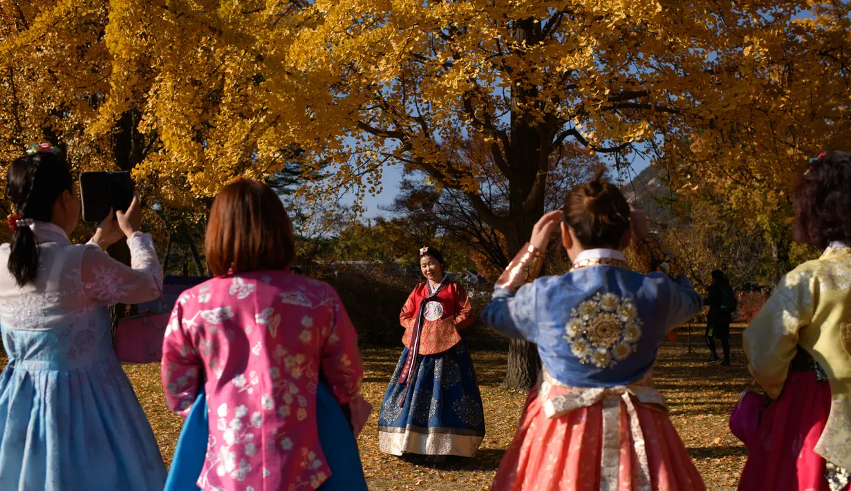 Pengunjung yang mengenakan pakaian tradisional hanbok berpose untuk foto di bawah pohon ginkgo di istana Gyeongbokgung di Seoul (31/10). Pohon Ginkgo yang berasal dari Tiongkok ini dikenal sebagai pohon rambut gadis. (AFP Photo/Ed Jones)