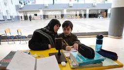 Serangan tersebut menyasar berbagai titik di wilayah perkotaan Lebanon, termasuk Beirut. Tampak dalam foto, seorang wanita Lebanon yang mengungsi duduk di samping seorang anak, mengawasi pelajaran daringnya melalui telepon seluler di sebuah sekolah negeri yang diubah menjadi tempat penampungan di kota Dekwaneh, utara Beirut, pada Rabu 25 Maret 2026. (Anwar AMRO/AFP)