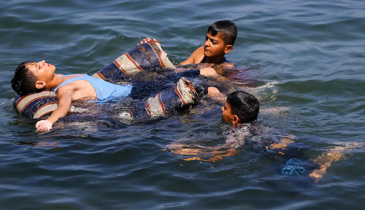Seorang anak laki-laki Palestina berbaring di kursi saat ia bermain bersama teman-temanya di laut Mediterania dekat kamp pengungsi al-Shati di Kota Gaza (3/7). (AFP Photo/Mohammed Abed)
