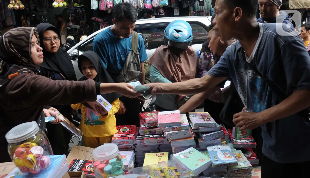 Pedagang buku tulis yang sedang sibuk melayani pembeli. (merdeka.com/Imam Buhori)