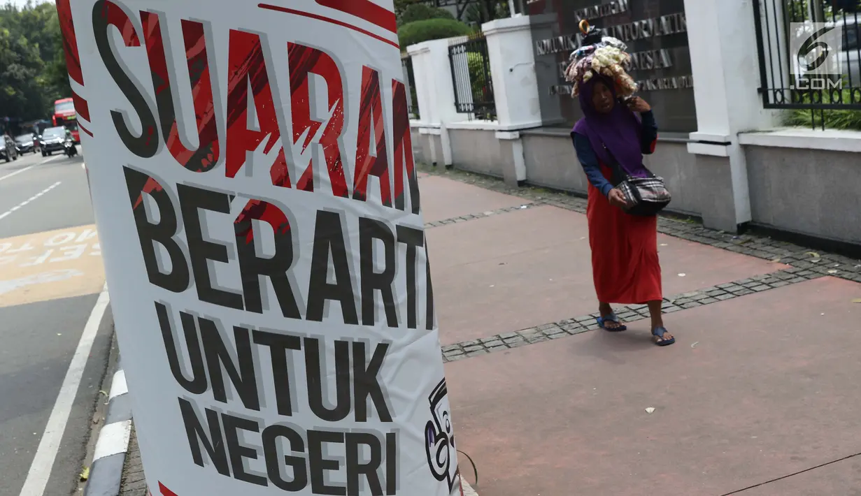 Pejalan kaki melintas di sisi media sosialisasi pelaksanaan Pemilu Serentak 2019 di depan kantor Kemenkominfo jalan Medan Merdeka Barat, Jakarta, Selasa (26/2). KPU menargetkan tingkat pemilih mencapai 77,5 persen. (Liputan6.com/Helmi Fithriansyah)