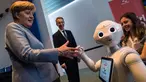 Kanselir Jerman Angela Merkel disapa robot interaktif di stand digitalSTROM selama pameran Girl's Day di Berlin, Rabu (26/4). Pameran ini bertujuan menarik wanita muda untuk menggeluti pekerjaan hi-tech dan engineering. (AFP PHOTO / John MACDOUGALL)