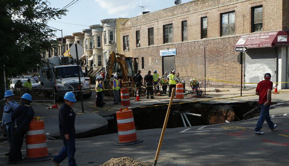 Sejumlah petugas bekerja di dekat lubang besar (sinkhole) di wilayah Brooklyn, New York, Selasa (4/8/2015). Lubang yang terbentuk di persimpangan pemukiman Sunset Park itu disebabkan erosi dan merusak pipa air serta aspal jalan. (AFP/Kena Betancur)
