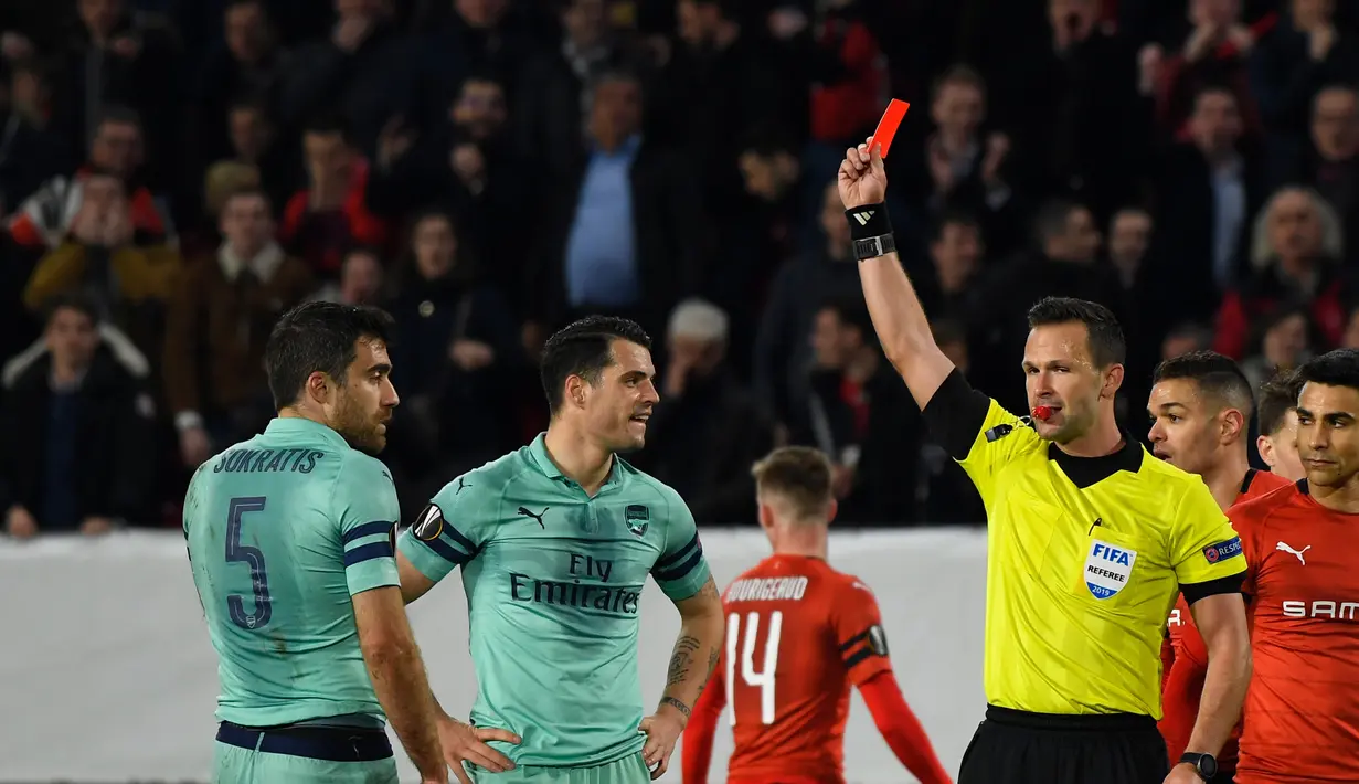 Wasit Ivan Kruzliac mengeluarkan kartu merah untuk Sokratis pada leg 1, babak 16 besar Liga Europa yang berlangsung di Stadion Roazhon Park, Rennes, Jumat (8/3). Arsenal kalah 1-3 kontra Rennes. (AFP/Damien Meyer)