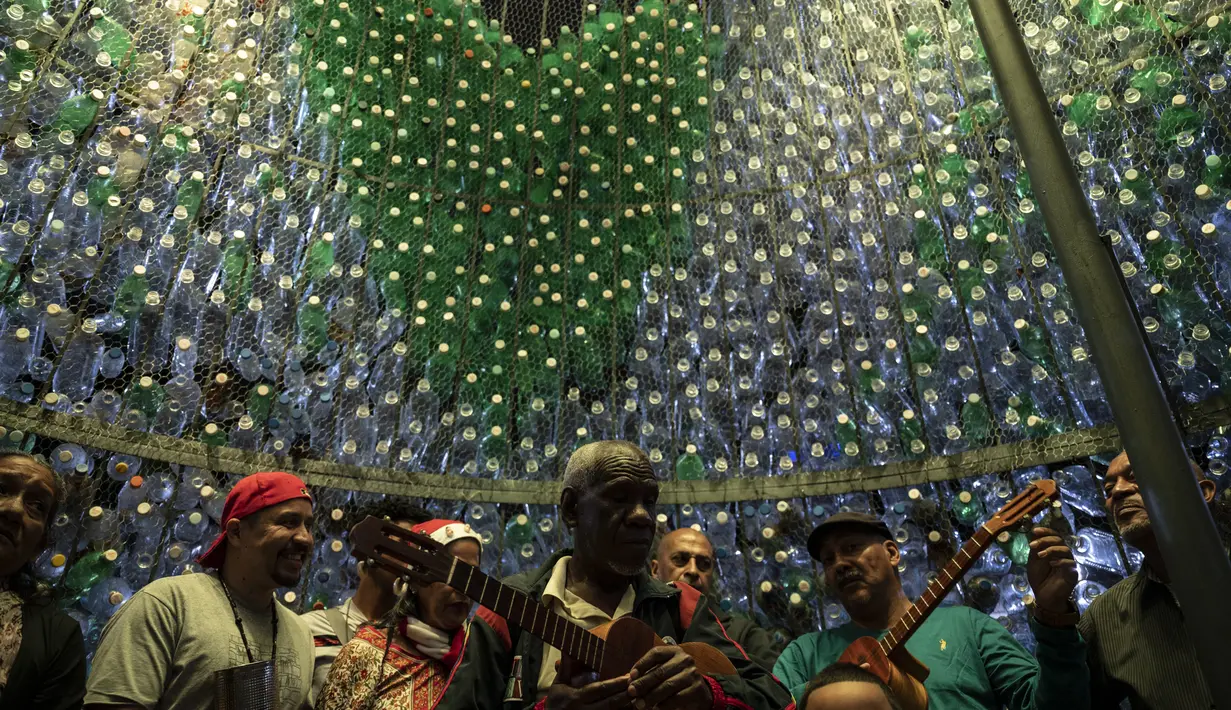 Musisi tetap berada di dalam pohon Natal yang terbuat dari botol plastik daur ulang di Caracas, Venezuela, Selasa (13/12/2022). Pohon Natal setinggi 10 meter tersebut merupakan proyek yang didukung kantor wali kota Caracas dan masyarakat umum yang berkontribusi dengan mengumpulkan botol dari jalanan. (Yuri CORTEZ / AFP)