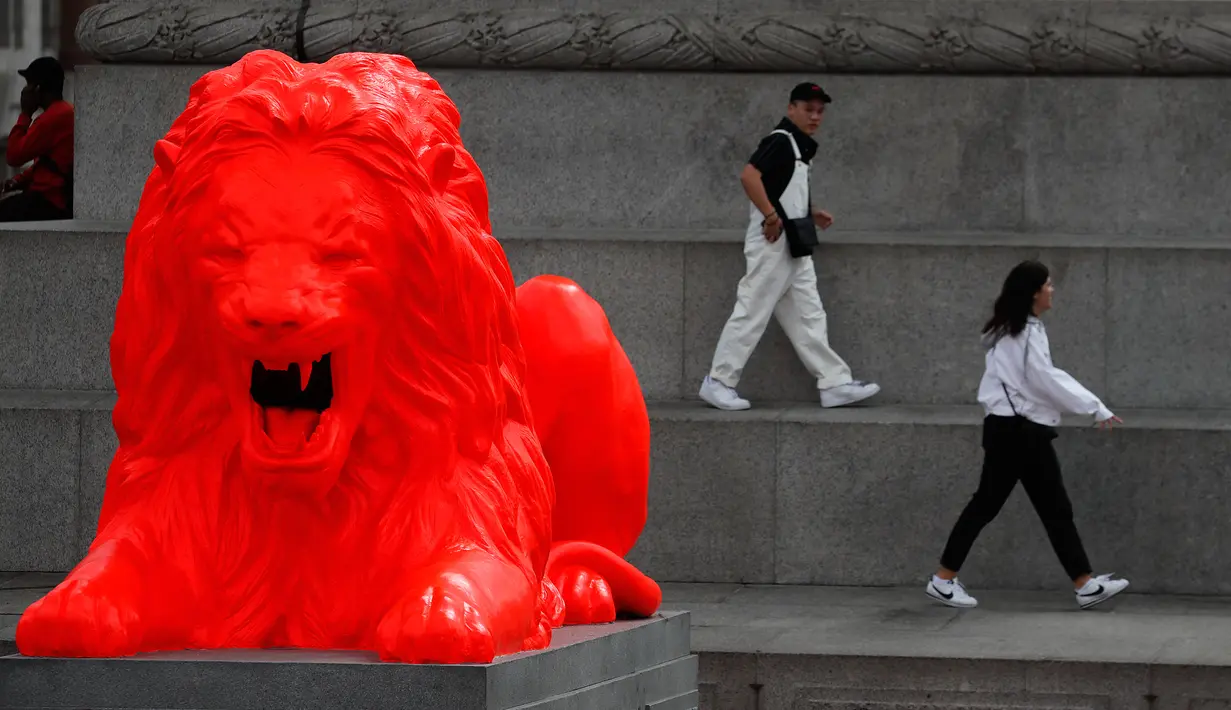 Wisatawan berjalan di dekat singa fluorescent merah yang bergabung dengan empat singa tradisional lainnya di Trafalgar Square di London (19/9). Patung Singa merah tersebut dipajang sebagai bagian dari Festival Desain London. (AP Photo/Frank Augstein)