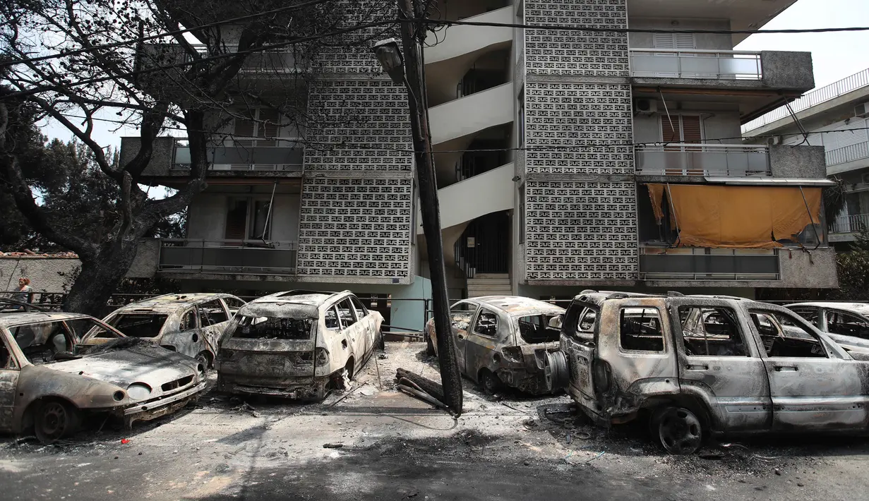 Mobil-mobil yang terbakar berdiri di luar blok apartemen di Desa Mati, timur Athena, Selasa (24/7). Tim penyelamat melaporkan menemukan lebih dari 20 jenazah berkerumun di dekat pantai. (AP Photo/Thanassis Stavrakis)