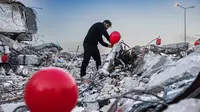 Ogun Sever Okur, pria Turki berusia 38 tahun menggantung balon di atas puing-puing bangunan yang runtuh di Antakya, Turki selatan pada 21 Februari 2023, menyusul gempa berkekuatan 6,4 yang melanda pada 20 Februari, dua minggu setelah gempa berkekuatan 7,8 gempa berkekuatan besar melanda dekat Gaziantep dan telah menewaskan lebih dari 44.000 orang. (AFP/Sameer Al-Doumy)