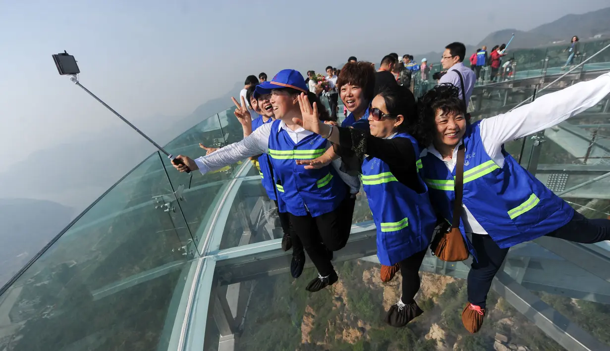 Pengunjung berfoto bersama di atas panggung berlantai kaca yang berada di pinggir tebing di Shilinxia, Beijing, 30 april 2016. Panggung kaca yang menggantung hingga 32.8 meter dari tepi tebing ini merupakan objek wisata baru di China. (AFP PHOTO/STR)