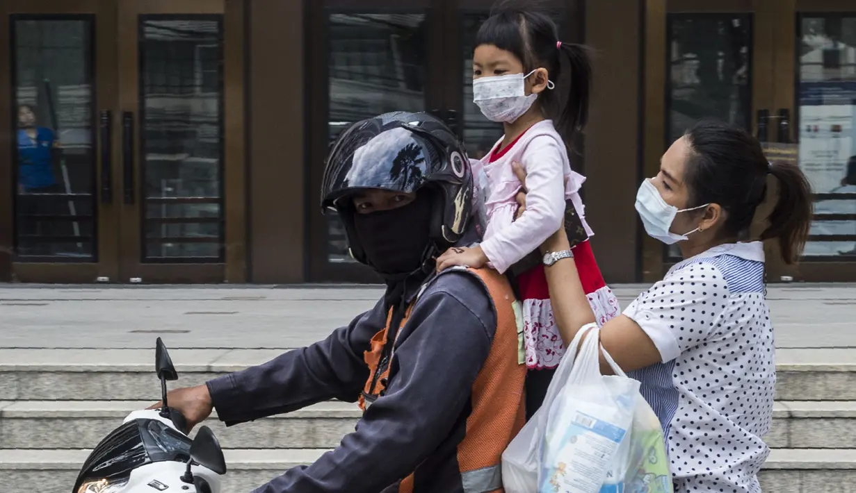 Seorang wanita bersama anaknya mengenakan masker saat menaiki motor saat kabut asap menyelimuti Bangkok (16/1). Thailand telah berupaya untuk mengatasi polusi yang telah menyelimuti ibukota dalam beberapa pekan terakhir. (AFP Photo/Romeo Gacad)