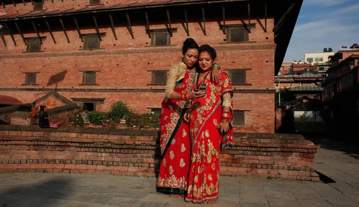 Dua wanita Hindu Nepal melihat ponsel setelah berswafoto di kuil Pashupatinath saat festival Teej di Kathmandu, Nepal, Kamis (24/8). Teej adalah festival paling terkenal di kalangan wanita Nepal. (Niranjan Shrestha/AP)