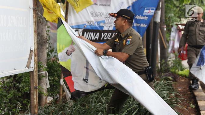 Petugas Satpol PP menurunkan APK yang terpasang di Jalan Raya Bogor dekat GOR Ciracas, Jakarta, Rabu (23/1). Penurunan APK ini karena pemasangannya dianggap melanggar ketentuan. (Liputan6.com/Helmi Fithriansyah)