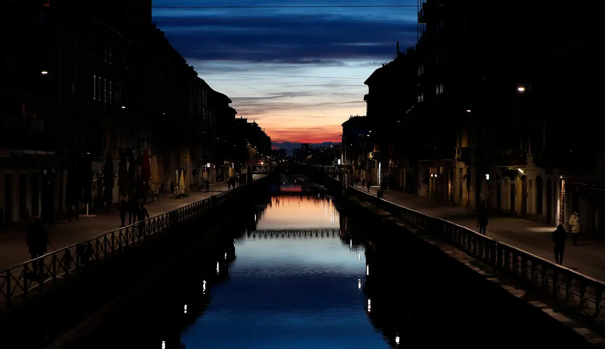 Beberapa orang berjalan di Kanal Naviglio Grande, Milan, Italia, Selasa (10/3/2020). Tak seperti biasanya yang selalu ramai, merebaknya virus corona (COVID-19) membuat salah satu tempat favorit bagi kehidupan malam di Milan tersebut kini terlihat sepi. (AP Photo/Antonio Calanni)
