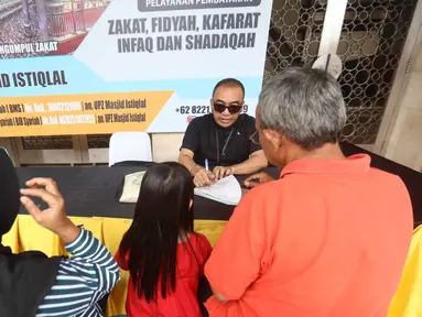 Petugas Unit Pengelola Zakat (UPZ) melayani pembayaran zakat, fidyah, kafarat, infaq, dan shadaqah di teras Masjid Istiqlal, Jakarta, Minggu 15 Maret 2026. Selain menjalankan ibadah selama bulan suci Ramadan, umat muslim juga diwajibkan untuk menunaikan zakat fitrah. (Kapanlagi.com/Budy Santoso)