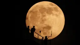 Siluet orang-orang saat bulan hampir purnama muncul di atas langit di Grozny, Rusia, Minggu (15/5/2022). (AP Photo/Musa Sadulayev)