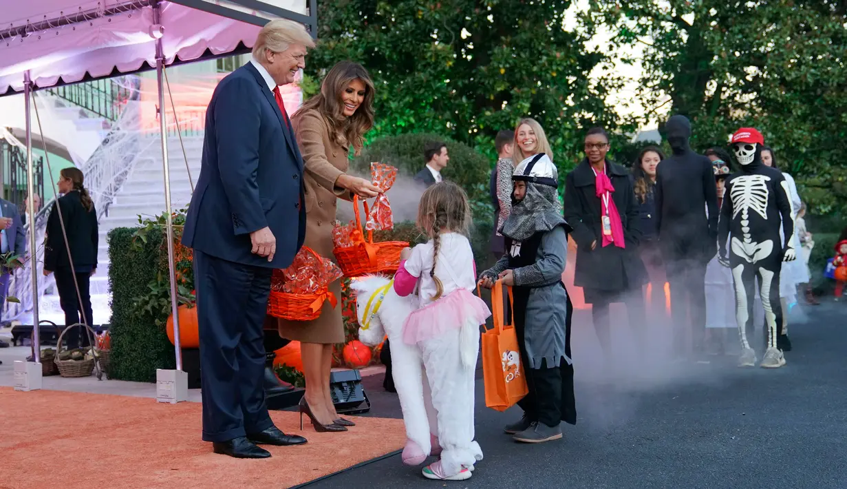 Presiden AS, Donald Trump dan Ibu Negara, Melania Trump membagikan permen kepada anak-anak saat open house perayaan pesta Halloween di Gedung Putih, Senin (30/10). Para siswa dan orang tua dari 20 sekolah hadir di acara ini. (AP/Pablo Martinez Monsivais)