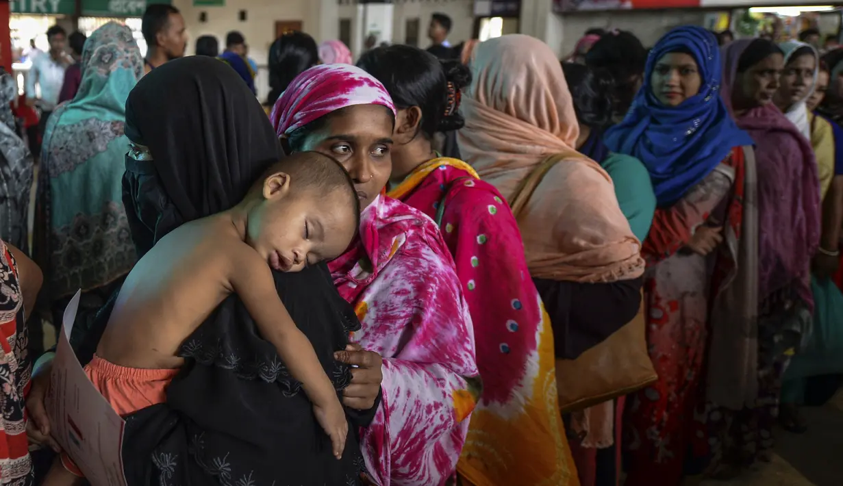 Seorang wanita menggendong anaknya saat mengantre membeli tiket menjelang Hari Raya Idul Adha 1440 H di sebuah stasiun kereta api di Dhaka (2/8/2019). Di Indonesia Idul Adha jatuh pada Minggu, 11 Agustus mendatang. (AFP Photo/Munir Uz Zaman)