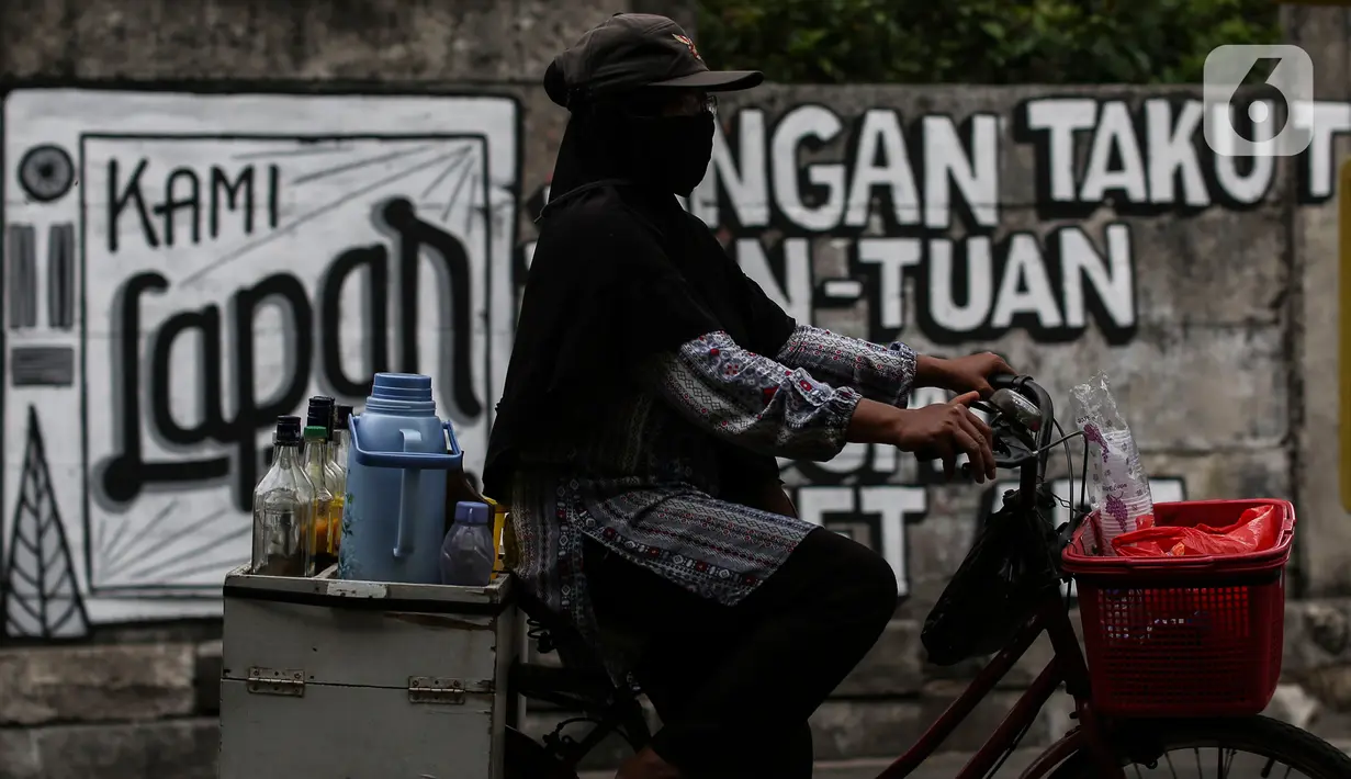 Penjual jamu melintasi mural bertuliskan “Kami Lapar Tuhan” di kawasan Jakarta Pusat, Selasa (24/8/2021). Mural 'Tuhan Aku Lapar' yang viral di jagat maya pada akhir Juli 2021 lalu, membuka rentetan peristiwa penghapusan mural di kota-kota besar Indonesia. (Liputan6.com/Johan Tallo)