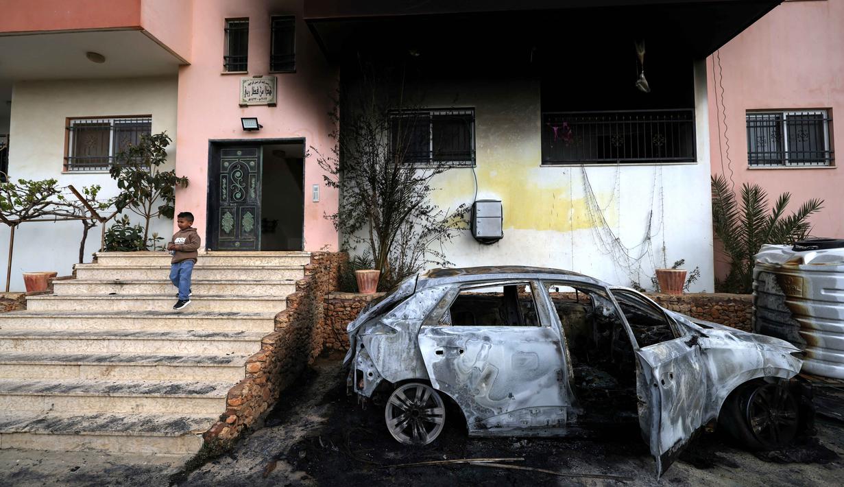 Seorang anak Palestina berdiri di sisi mobil yang hancur dan di luar rumah yang terbakar setelah serangan yang dilaporkan dilakukan oleh pemukim Israel di desa Deir al-Hatab, sebelah timur kota Nablus, di Tepi Barat, wilayah yang diduduki Israel pada Senin 23 Maret 2026. Penyerangan yang dilakukan pemukim ilegal Israel di Tepi Barat terhadap warga Palestina kembali terjadi. (JAAFAR ASHTIYEH/AFP)