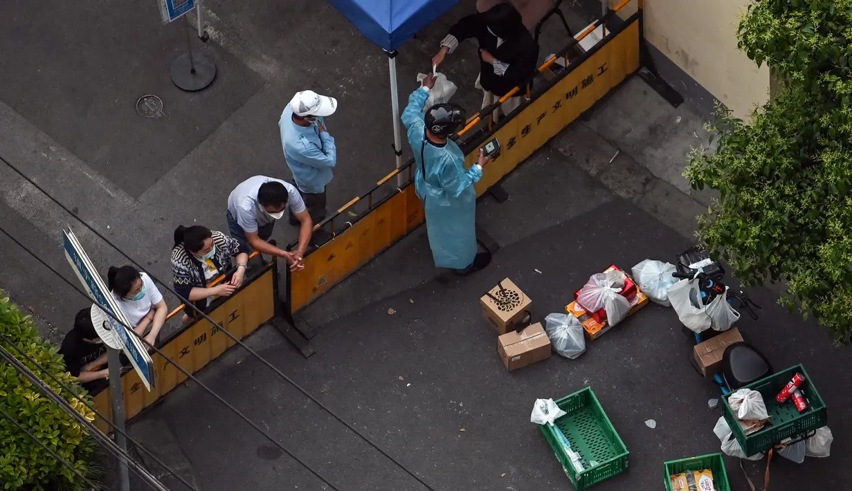Seorang penduduk mengumpulkan makanan dari seorang pekerja pengiriman di sebuah pos pemeriksaan pada jalan yang ditutup saat pemberlakuan lockdown karena virus corona COVID-19 di Distrik Jing'an, Shanghai, China, Selasa (17/5/2022). (Hector RETAMAL/AFP)