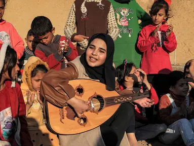 Ruaa Hassouna memainkan alat musik Oud untuk anak-anak Palestina mereka di Rafah, Selatan Jalur Gaza, 18 Desember 2023. (SAID KHATIB/AFP)