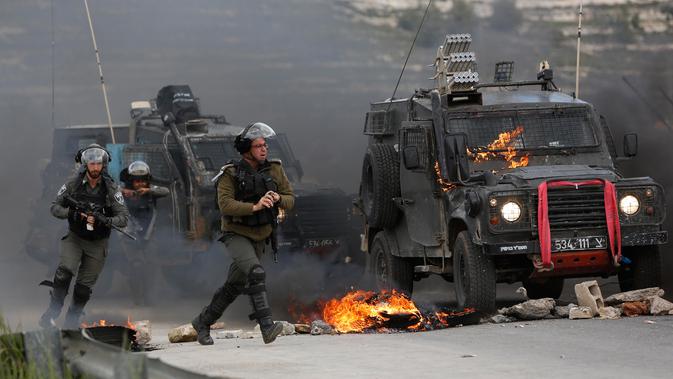 Tentara Israel mengejar pengunjuk rasa saat kendaraan militer mereka terbakar oleh lemparan bom molotov warga Palestina di pinggiran Kota Ramallah, Tepi Barat, Rabu (27/3). Bentrokan ini sebagai bentuk protes terhadap tahanan Palestina yang berada di Israel. (AP Photo/Majdi Mohammed)