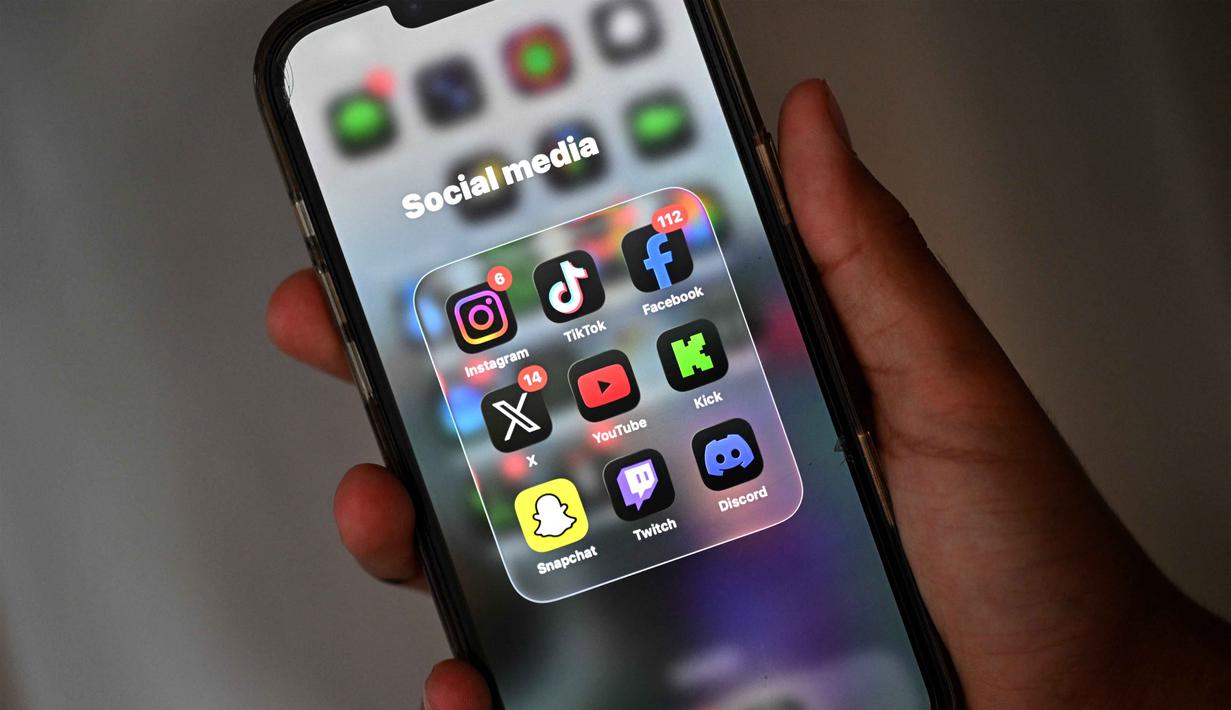 Peraturan ini juga mewajibkan platform media sosial untuk memblokir pengguna di bawah umur atau menghadapi denda yang signifikan. Tampak dalam foto, seorang anak laki-laki berusia 13 tahun berpose di rumahnya sambil melihat media sosial di ponselnya di Sydney, Australia pada Senin 8 Desember 2025. (Saeed KHAN/AFP)