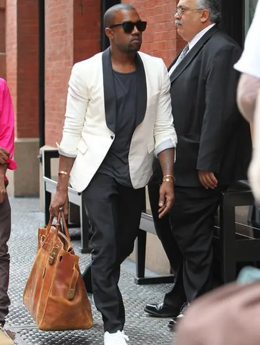 Kanye West terlihat sedang menenteng tas Hermes Birkin versi jumbo bernuasa cokelat. Tampilan kasual dengan blazer putih dipadu t-shirt dan celana panjang hitam, serta sepatu kets putih. Foto: Website.