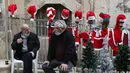 Orang-orang duduk di depan sejumlah kostum Sinterklas yang dipajang di dekat sebuah toko di Kota Tua Yerusalem (7/12/2020). (Xinhua/Muammar Awad)