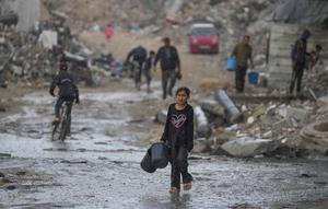 Seorang anak perempuan membawa dua ember kosong saat berjalan menuju tempat mengambil air di tengah hujan deras di kawasan Sheikh Radwan, Kota Gaza, Jumat 14 November 2025. Anak-anak di Gaza masih mengalami kekurangan air bersih. (AP Photo/Jehad Alshrafi)