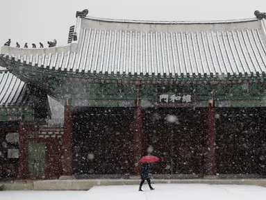 Seorang wanita menggunakan payung  berjalan saat hujan salju di Istana Gyeongbok di Seoul, Korea Selatan (13/12). Istana Gyeongbok merupakan kerajaan utama selama Dinasti Joseon dan salah satu landmark terkenal di kota tersebut. (AFP Photo/Lee Jin-man)