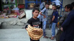 Seorang anak menerima roti gratis dari kota selama lockdown untuk mencegah penyebaran virus corona, pada bulan suci Ramadan di Kabul, Afghanistan (4/5/2020). Muslim di seluruh dunia sedang menjalankan Ramadan, ketika mereka menahan diri dari makan, minum dari subuh hingga senja. (AP/Rahmat Gul)