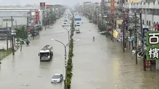 Orang-orang dan kendaraan menyeberangi air di sepanjang jalan yang tergenang banjir akibat Topan Gaemi di Kaohsiung, Taiwan pada tanggal 25 Juli 2024. ((Johnson LIU/AFP)