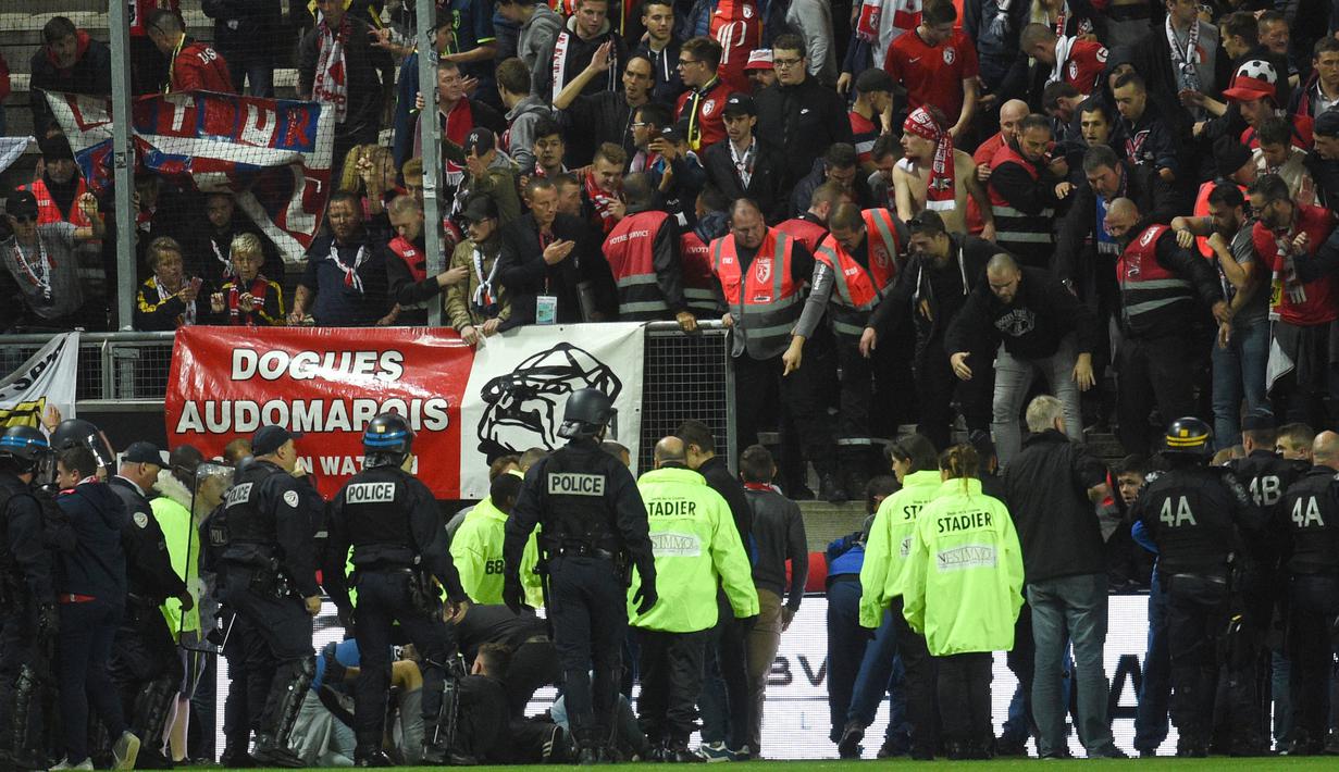 Petugas keamanan membatu suporter yang terjatuh dari tribun saat Amiens melawan Lille LOSC  di Licorne stadium, Amiens, (30/9/2017). Laga tersebut akhirnya ditunda. (AFP/Francois Lo Presti)
