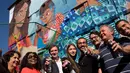 Seniman Brasil, Luna Buschinelli berpose dengan latar belakang mural berjudul 'Contos' di dinding gedung sekolah Rio de Janeiro, (19/6). Mural itu mengisahkan seorang ibu buta huruf yang sedang membacakan buku cerita ke anak-anaknya. (AP/Silvia Izquierdo)