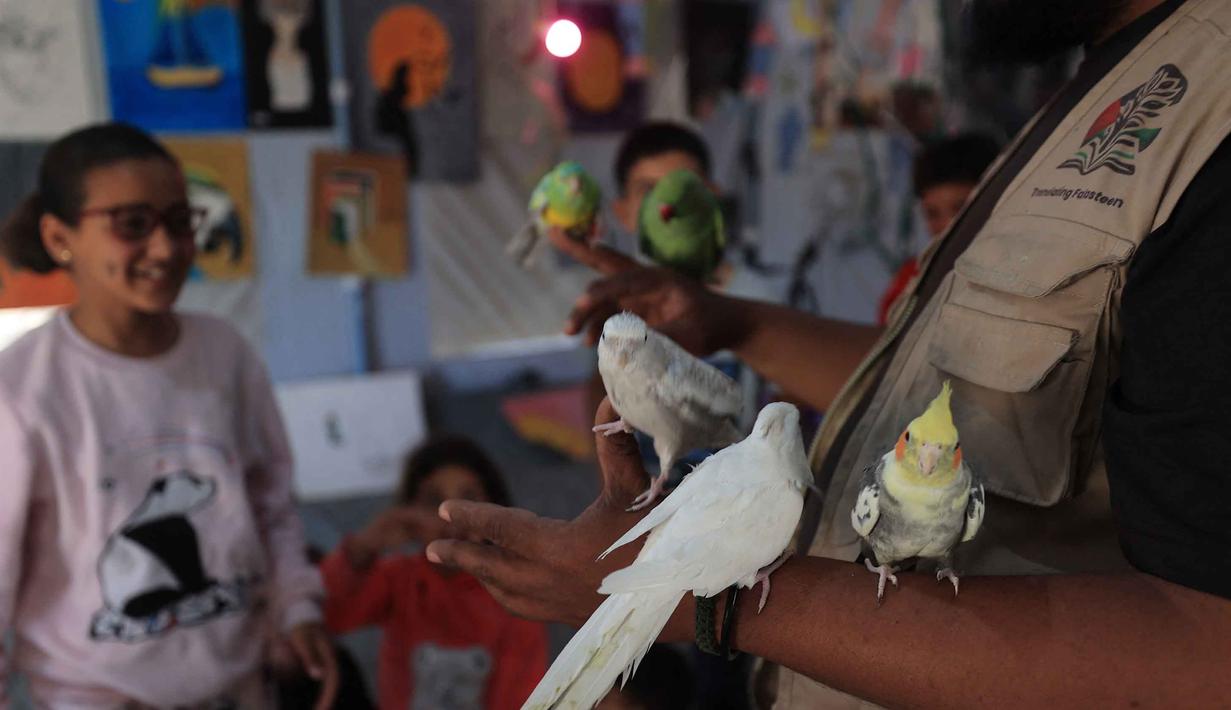 Bersama para relawan, anak-anak pengungsi Palestina bermain bersama beberapa hewan peliharaan dan burung di dalam sebuah tenda studio seni sederhana. Tampak dalam foto, anak-anak pengungsi Palestina mengikuti sesi konseling psikologis di sebuah studio seni yang menggunakan hewan peliharaan dan burung di daerah Al-Zawaida, Jalur Gaza Tengah, pada Selasa 21 April 2026. (Eyad Baba/AFP)