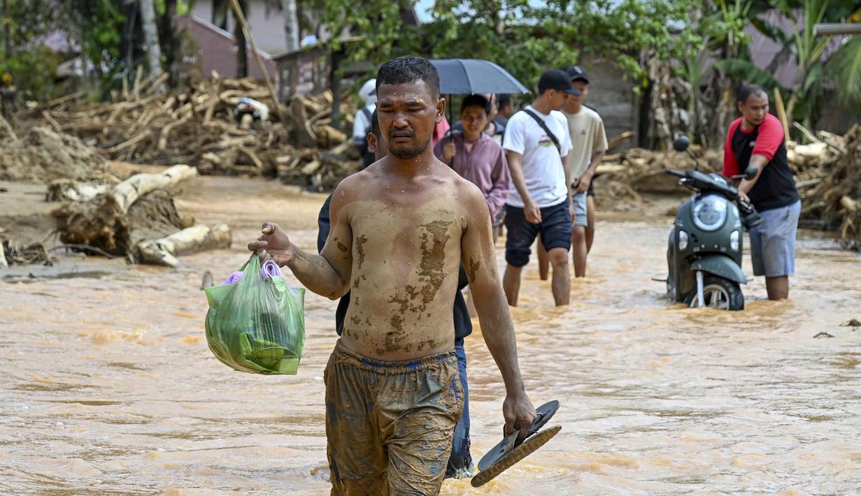 Sementara, data terbaru Badan Nasional Penanggulangan Bencana (BNPB) pada 2 Desember 2025, menyebut, secara keseluruhan, korban tewas akibat rangkaian banjir dan tanah longsor yang melanda sejumlah wilayah di Pulau Sumatera sejak pekan lalu telah mencapai 712 jiwa. Tampak dalam foto, warga berjalan di tengah banjir bandang di Desa Tukka, Tapanuli Tengah, Sumatera Utara, pada 2 Desember 2025. (YT HARIONO/AFP)