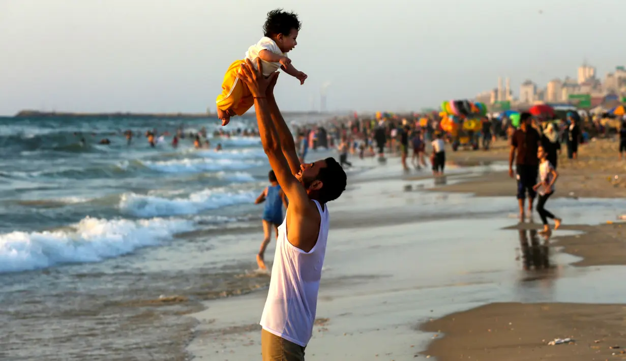 Seorang pria Palestina menggendong balita sambil menikmati pantai Kota Gaza, Jumat (22/6). Pantai Gaza menjadi pelipur bagi penduduk yang tak punya pilihan berwisata ke luar kota atau luar negeri. (AFP PHOTO/MAHMUD HAMS)