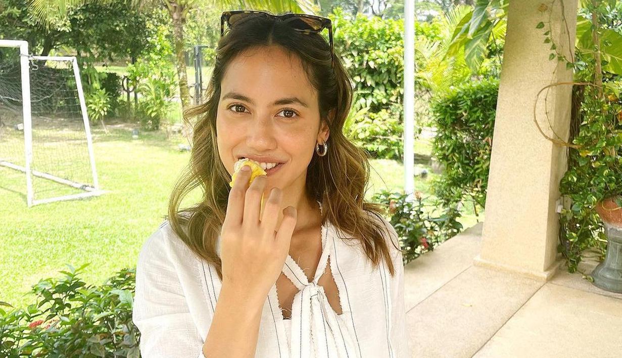 <p>Ekspresi Pevita Pearce saat pertama kali makan durian. Di unggahan tersebut, Pevita terlihat memakai baju berwarna putih dengan bawahan batik berwarna biru muda. Pevita tampil natural tanpa makeup dengan penuh senyum. (Instagram/pevpearce)</p>
