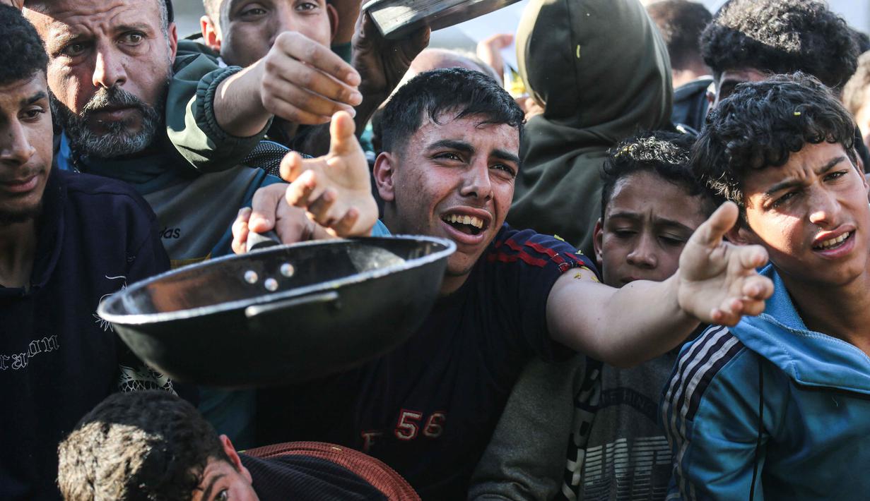 Warga Palestina yang mengungsi berebut untuk makanan di Khan Younis, selatan Jalur Gaza pada Jumat 6 Maret 2026. Krisis pangan di Gaza kembali mencapai titik kritis. Situasi ini imbas eskalasi konflik regional yang memicu penutupan seluruh pintu perlintasan perbatasan ke Gaza oleh Israel. (Bashar Taleb/AFP)